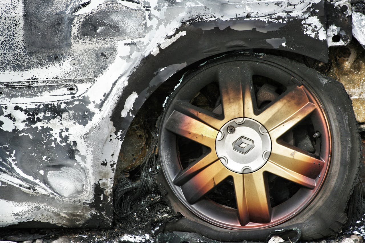 contact-img Detailed shot of a burned car wheel with rusty mag and damaged tire, showing fire aftermath.
